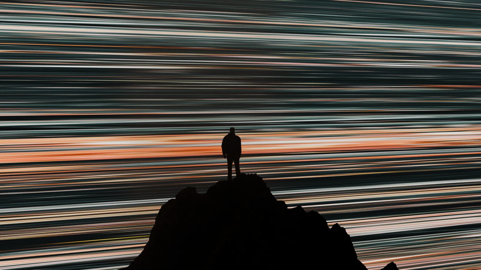 A lone figure on a peak beneath streaking light